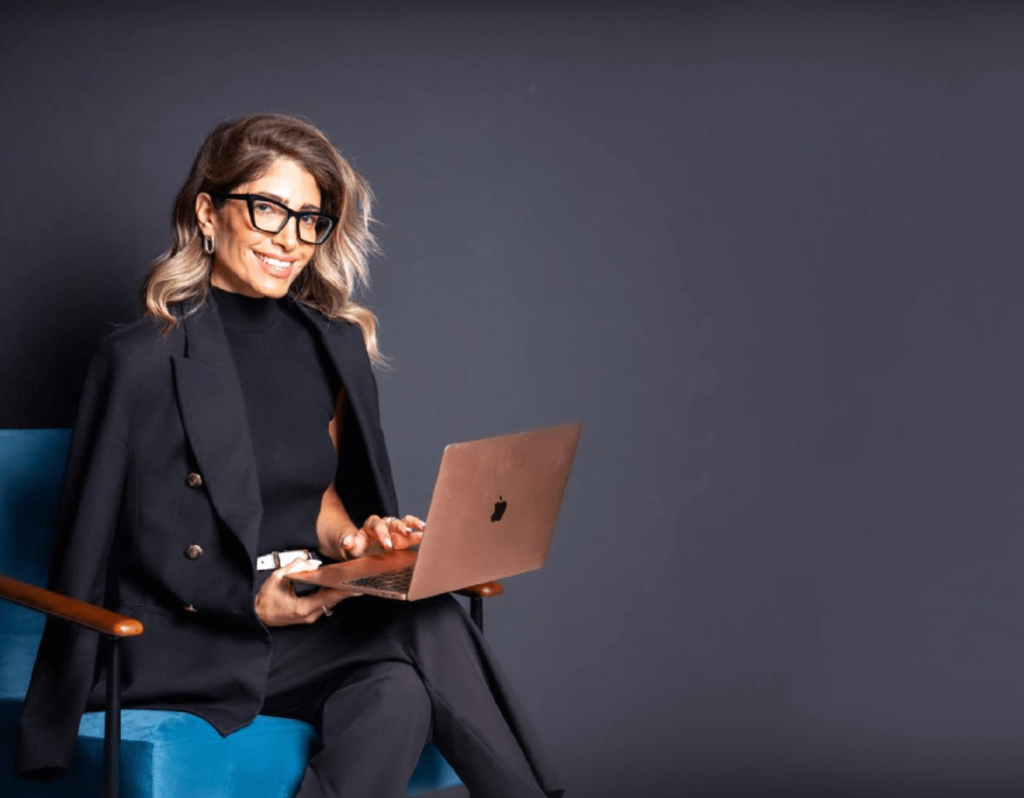 מעיין ברנע יושבת עם מחשב על רקע קיר אפור